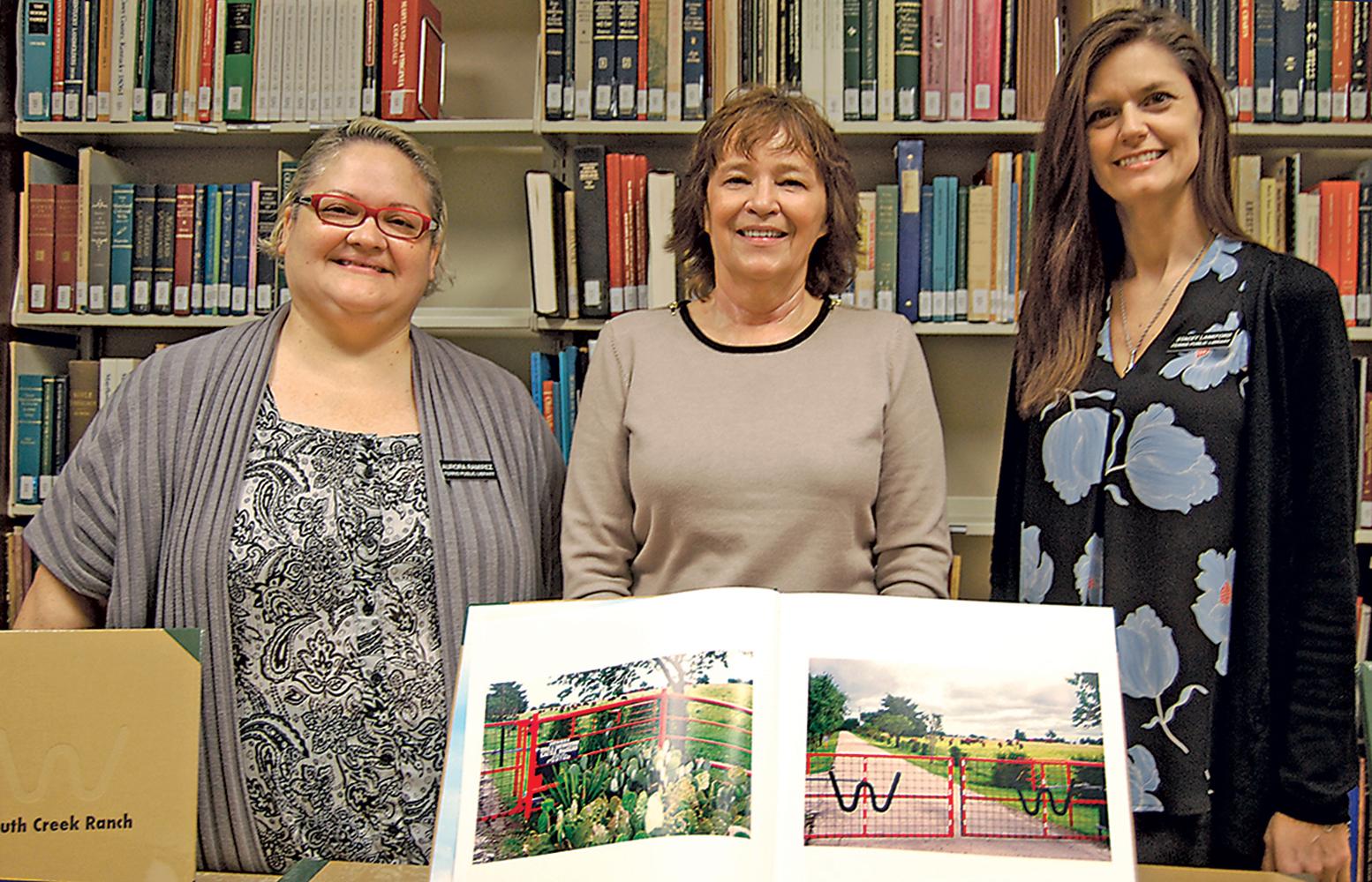 Shown displaying one the colorful  books depicting the beauty and history of South Creek Ranch in Ferris are Aurora Eamirez, Kathy Harrington, librarian and Stacy Lankford. Benefactor Bea Wallace donated the books for a library fundraiser. Wallace is the widow of Ray Wallace. Together they built 6,300-acre estate includin a four-story, 23,000 sq. foot mansion. The price of the books are yet to be determined. The library is located at 301 W. 10th St and can be reached by calling 972-544-3696.