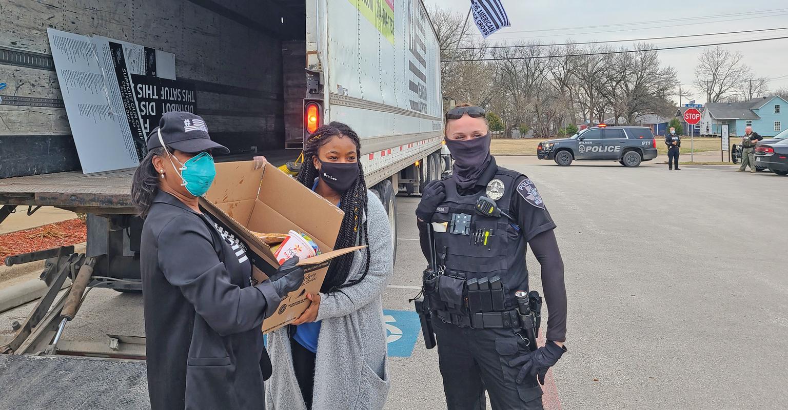 American Black Cross’s Debbie Walker, Charitee Higgins from State Representative Sherman’s office, and a Wilmer police officer hold a box of food given to Wilmer residents. 