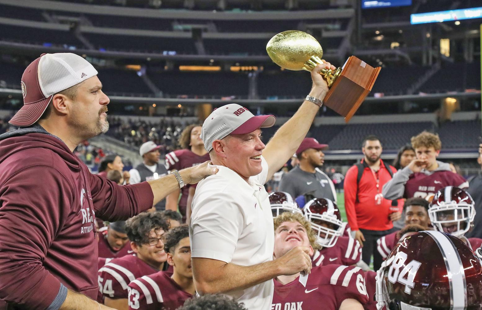 Head Coach Chris Ross hoists the Area Round Championship trophy over his Hawks football team at AT&T Stadium.